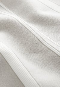 Tissu gris clair avec une texture à fine côtes et des coutures surélevées. Le matériau semble doux et légèrement extensible, présentant des variations subtiles de teinte.