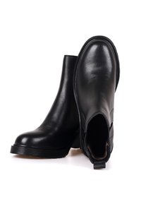 Czarne skórzane botki za kostkę o gładkim wykończeniu, zaokrąglonym nosku i elastycznych panelach bocznych. Zawierają niską, teksturowaną gumową podeszwę oraz uchwyt.