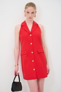Abito rosso senza maniche con colletto, bottoni dorati e due tasche frontali. Abbinato a una piccola borsa nera a tracolla. Tessuto dalla texture liscia.