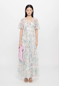 Lichte, bloemrijke maxi-jurk met gelaagde ruffles in pastelkleuren. Doorzichtige stof met pofmouwen. Vergezeld van een roze accessoire.