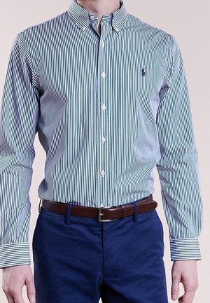 Blue and white striped cotton dress shirt with button-down collar and purple logo. Worn with blue pants and a brown belt.