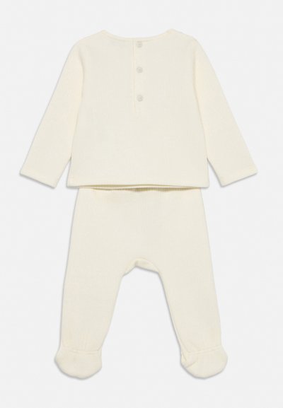 Kreemikass värvitoonis beebiriietus, pikkade varrukatega top, millel on taga kolm nuppu, ja jalaga püksid, mis on tehtud pehmest kangast.