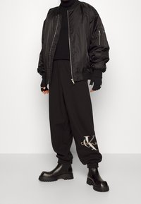 Svart bomberjacka med dragkedja, ribbade ärmslut, ihop med lösa svarta joggers med en guldig logga. Chunkiga svarta stövlar fulländar outfiten.