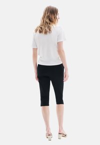 Camiseta blanca de manga corta combinada con pantalones negros cropped. La modelo lleva sandalias de tacón cuadrado beige. Diseño simple y limpio, sin patrones.