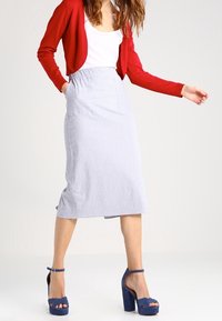 Blå og hvid stribet midi-nederdel med frontlommer, parret med en tætsiddende hvid top og en rød cardigan. Båret med blå platformhæle.