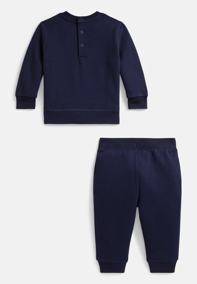 Μακρυμάνικη παιδική μπλούζα σε ναυτικό μπλε με τρία κουμπιά στην πλάτη και αντίστοιχο παντελόνι με ελαστική μέση και ρεβέρ στα πόδια.
