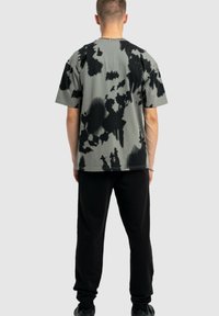 Koszulka z krótkim rękawem, luźna, w stonowanym odcieniu szarości z czarnym wzorem tie-dye. Noszona z czarnymi spodniami i trampkami.