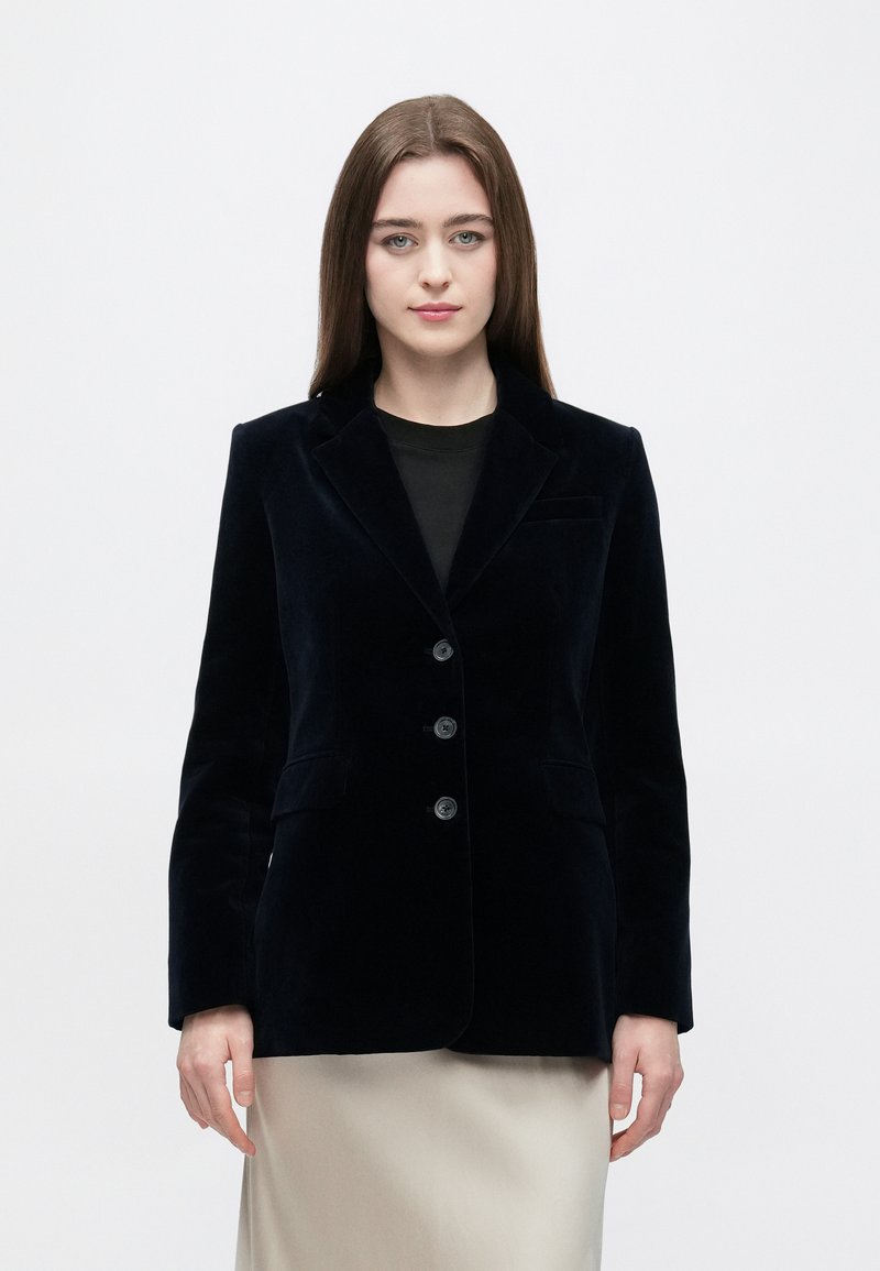 Blazer in velluto blu navy con design strutturato, chiusura monopetto, rever a incavo e tre bottoni. Presenta tasche laterali e una texture liscia.
