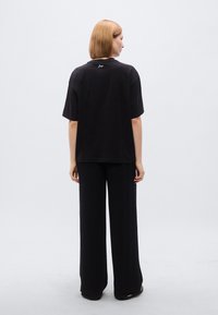 Μαύρο βαμβακερό μπλουζάκι με άνετη εφαρμογή, κοντά μανίκια και στρογγυλή λαιμόκοψη. Συνδυάζεται με μαύρο παντελόνι φαρδιάς γραμμής που ταιριάζει.