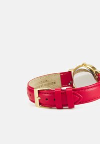 Roter Lederuhrarmband mit goldfarbener Metallschließe, runder Gehäuseform und klarem Glas. Besitzt eine eingeprägte Genuine-Leder-Beschriftung auf der Innenseite.