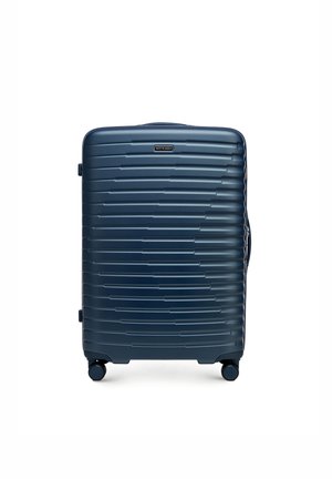 Twarda walizka w kolorze granatowym, z teksturowaną powierzchnią i poziomymi rowkami, zintegrowanymi kółkami oraz bocznym uchwytem ułatwiającym przenoszenie.