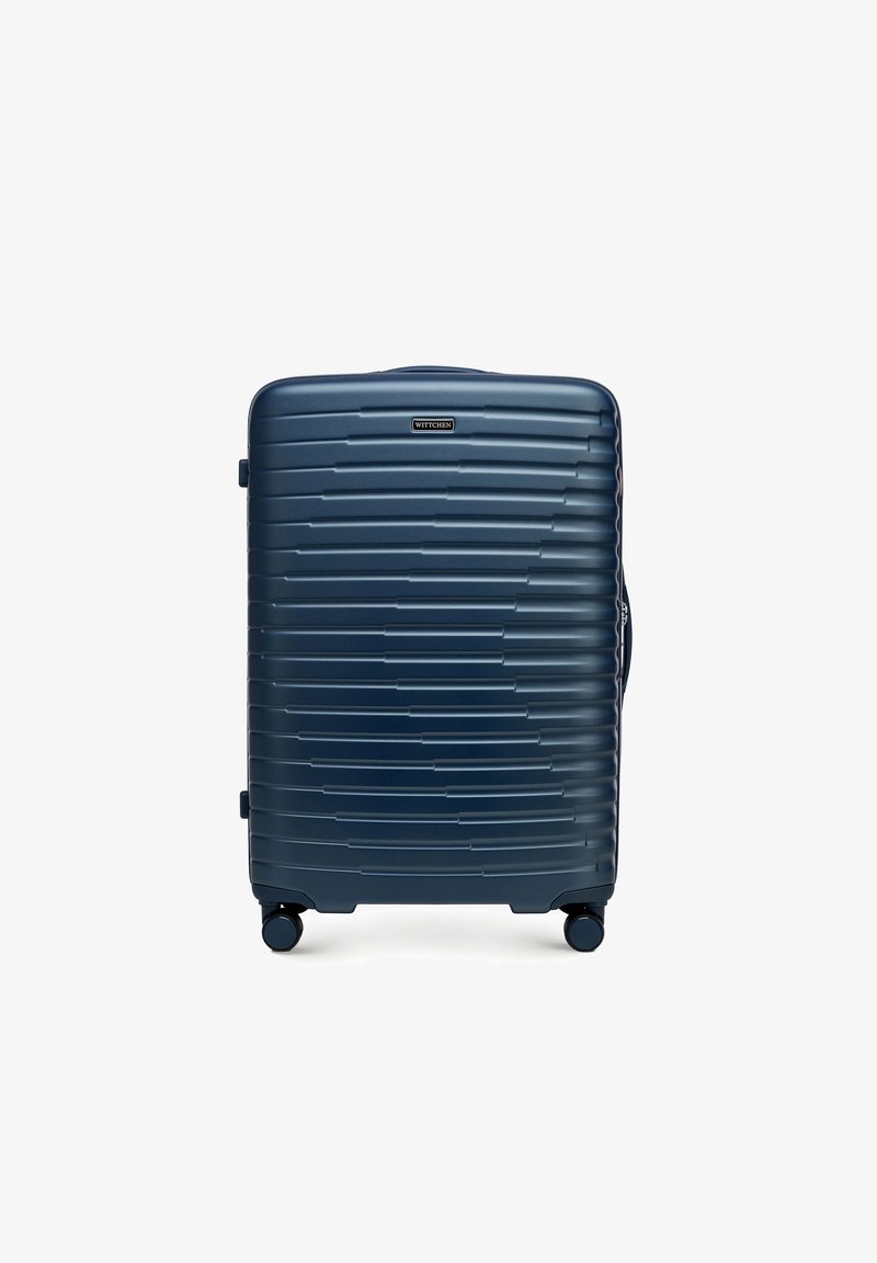 Valise rigide en bleu marine, présentant une surface texturée avec des rainures horizontales, des roues intégrées et une poignée latérale pour faciliter le transport.