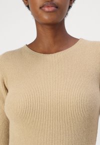 Maglione a costine beige con scollo rotondo e silhouette aderente, che mette in evidenza una morbida texture e un dettagliato motivo verticale.