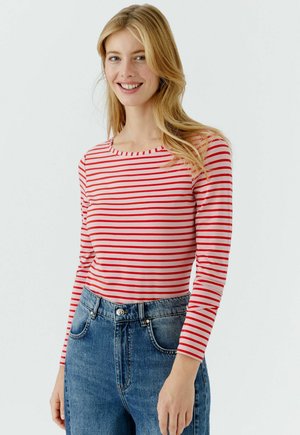 Chemise à manches longues rayée rouge et blanche en tissu léger, avec un col rond et un design épuré, assortie à un jean bleu taille haute.