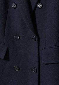 Blazer in lana blu navy con design doppiopetto, bottoni neri e tasche a lato. Tessuto liscio con rever strutturati.