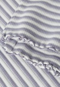 Materiał w paski w kolorach lawendy i bieli, z teksturowanym splotem prążkowanym. Krawędzie zdobi delikatna falbana, dodająca subtelnej głębi.