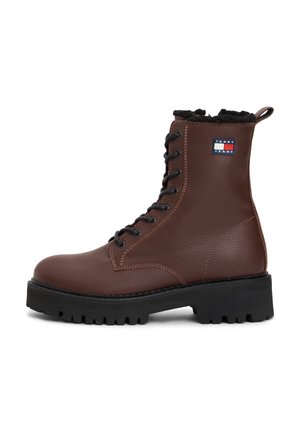 Brun læder snørestøvle til anklen med sort chunky sål og sort pelsforing, med et Tommy Jeans logo mærke på siden.