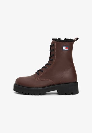 Bottine marron en cuir à lacets, semelle noire épaisse et doublure en fourrure noire, avec un patch logo Tommy Jeans sur le côté.