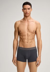 Harmaat puuvillaiset bokserishortsit, joissa kuvioitu joustava vyötärönauha. Tiukka istuvuus, sileä pinta ja reiden puoliväliin ulottuva pituus. Ei näkyviä logoja tai koristeita.