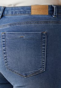 Temno modri jeans iz denim materiala z zadnjim žepom s vidnimi šivi in tanjšim usnjenim etiketom na pasu, ki navaja "ONLY CARMAKOMA."