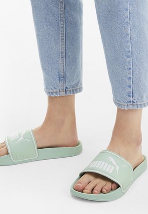 Des sandales glissantes vertes en caoutchouc avec une large sangle affichant le logo Puma. Le design présente une semelle plate et un bout ouvert.