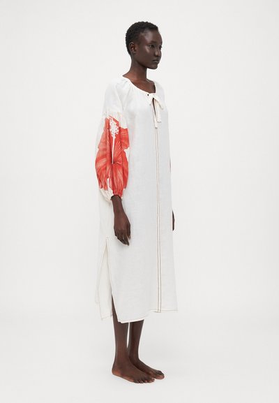 Weißes Leinenkleid mit legerer Passform, das ein lebhaftes rotes Blumenmuster auf den gepufften Ärmeln und einen seitlichen Schlitz aufweist, abgerundet mit einem Bindeband am Ausschnitt.