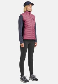 Gewatteerd mouwloos jack in roze met een ritssluiting aan de voorkant, gecombineerd met een marineblauw shirt met lange mouwen en zwarte leggings, als complete buitenkleding.
