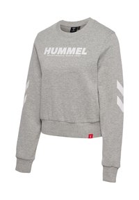 Lysegrå crewneck-sweatshirt med teksten "HUMMEL" på brystet, hvide chevron-striber på ærmerne og rød mærkat med mærke ved kanten.