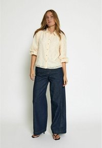 Light peach button-up shirt with a subtle wave pattern, paired with dark blue wide-leg jeans. Sandals complete the outfit.