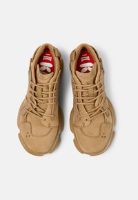 Tanfarbene Wildleder-Sneaker mit Schnürverschluss, runder Zehenpartie und Gummisohle. Mit rotem und weißem Logo auf der Innensohle und gepolsterter Schuhzunge.