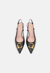Pantofi slingback din piele neagră cu vârf ascuțit și o cataramă decorativă aurie, având o textură netedă și o branț bej.