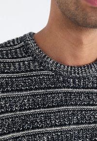 Strickpullover in Marineblau und Weiß, mit einem strukturierten Muster und horizontalen Streifen. Runder Kragen und gerippte Ränder.
