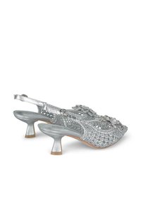 Tacchi slingback intrecciati argento con tacco conico basso, accenti floreali decorativi e dettagli testurizzati sulla tomaia.