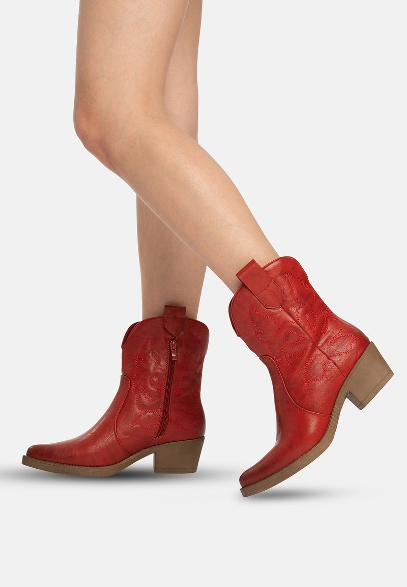 Gambe con stivali da cowboy in pelle rossa a metà polpaccio, con cerniera laterale e cuciture decorative, tacchi bassi beige a blocco.