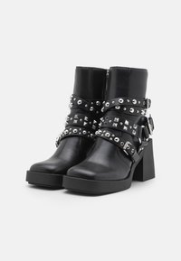 Black leather ankle boots with chunky heels, adorned with silver studs and straps. Side zipper closure enhances the edgy design.