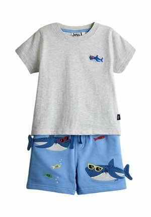 Helehall lühikeste varrukatega särk, mille rinnal on väike hai, ja sinised lühikesed püksid, millel on päikeseprillidega hai ja väikeseid värvilisi kalu.