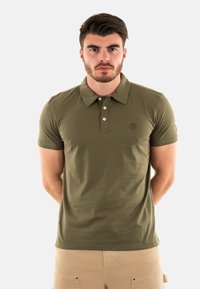 Polo-shirt vert olive en coton, avec un col, une patte de boutonnage à trois boutons et un logo discret sur la poitrine.
