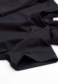 Černé tričko vyrobené z měkké a elastické tkaniny. Má kulatý výstřih a krátké rukávy. Okraje mají čistý, šitý vzhled.