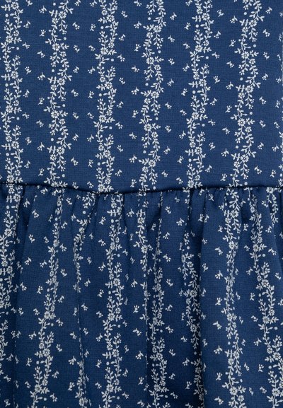 Ναυτικό ύφασμα με λευκό floral σχέδιο. Το σχέδιο περιλαμβάνει κατακόρυφους βλαστούς και μικρά φύλλα, με συγκεντρωμένη υφή στο κάτω μέρος.