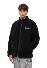 Czarna polarowa kurtka z wysokim kołnierzem i zapięciem na zamek. Na froncie haft "wild side" w kolorze białym. Teksturowany, miękki materiał; luźny krój.
