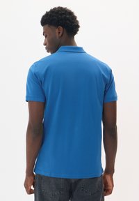 Polo azul con cuello y mangas cortas, hecho de algodón. La parte trasera presenta una textura suave y un dobladillo recto.