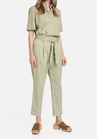 Jasnozielona, krótki rękaw, koszula z guzikami z przodu, związana w talii oraz spodnie w luźnym, plisowanym kroju. Beżowe klapki na drewnianych obcasach.
