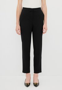 Zwarte op maat gemaakte broek met een gladde stof, rechte snit en een platte tailleband. Gekenmerkt door het combineren met zwarte puntige hakken met gouden accenten.