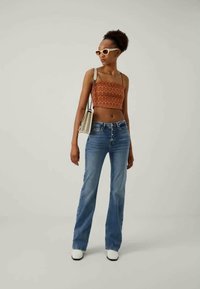 Λευκά γυαλιά ηλίου, ένα κοντό καφέ καρό τοπ και ανοιχτό μπλε φαρδιά τζιν. Το μοντέλο κρατάει μια λευκή τσάντα και φοράει λευκή υπόδηση.