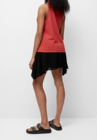 Rød ærmeløs top parret med en sort, tekstureret asymmetrisk nederdel og sorte sandaler. Outfittet har et afslappet og lagdelt design.