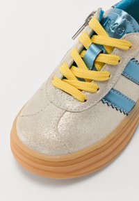 Silver, glittery sneaker with blue stripes, yellow laces, and a glossy blue tongue. Features a zipper detail and a rubber sole.