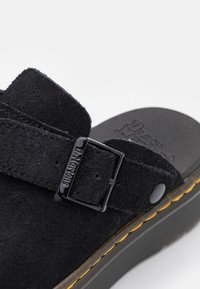 Sandal in suede nero con cinturino regolabile a fibbia, parte superiore testurizzata e suola nera ammortizzata con accenti di cucitura gialla.