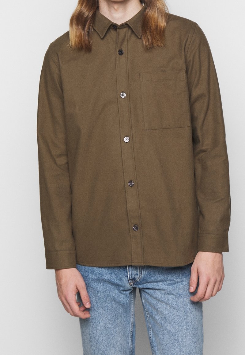 Chemise marron à manches longues en tissu texturé, avec une fermeture boutonnée à l'avant, un col pointu et une poche poitrine.