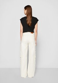 Top negro de manga corta con capucha combinado con pantalones cargo de pierna ancha de talle alto en color blanco roto, que cuentan con bolsillos laterales y una etiqueta de cuero en la cinturilla.