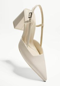 Chaussure à talon haut en cuir verni beige avec un bout pointu, un talon bloc et une sangle de cheville dotée d'une boucle en métal argenté pour l'ajustement.
